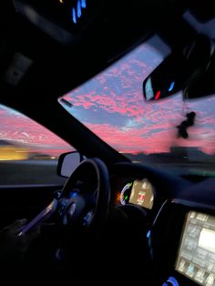 the inside of a car driving down a road at dusk with pink clouds in the sky