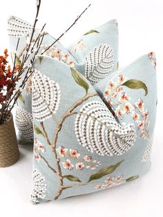 two decorative pillows sitting next to each other on top of a white table with flowers in vases