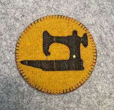 a yellow and black patch with a sewing machine on it's side in the shape of a button