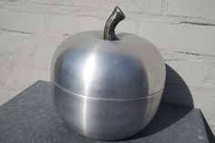 a metal apple sitting on top of a cement slab next to a white brick wall