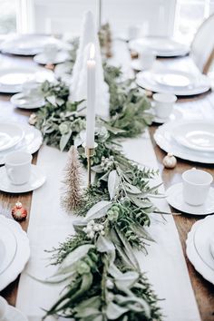 the table is set with white plates and greenery, candlesticks and silverware