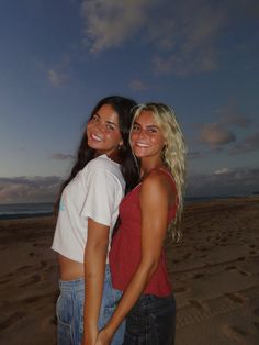 two young women standing next to each other on a beach at night with the sky in the background