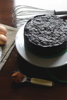 a chocolate cake sitting on top of a white plate next to eggs and whisks