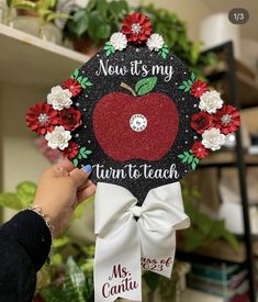 someone is holding up a graduation cap with an apple on it that says now it's my turn to teach