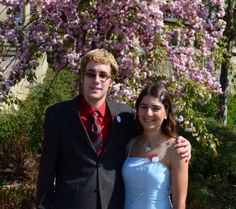 a young man and woman posing for a photo in front of a tree with pink flowers