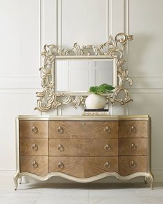 a white vase sitting on top of a wooden dresser next to a large gold mirror