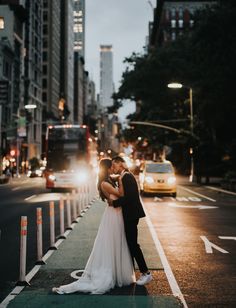 a bride and groom kissing on the street in new york city at night with skyscrapers in the background