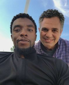 two men are posing for the camera in front of a blue sky and white clouds