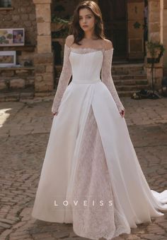 a woman in a white wedding dress standing on a cobblestone walkway wearing an off - the - shoulder gown