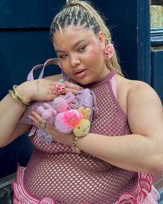 a woman with braids and pink dress holding a stuffed animal in her hand while standing next to a blue door