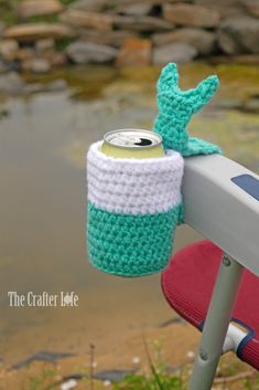 a crocheted can holder sitting on top of a red chair next to a body of water