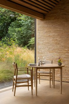 a wooden table and chairs in front of a brick wall with glass doors leading outside