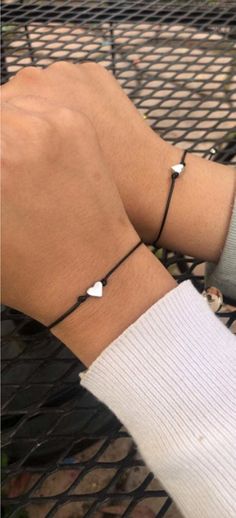 a person wearing two bracelets on their wrist, one with an arrow and the other with a heart