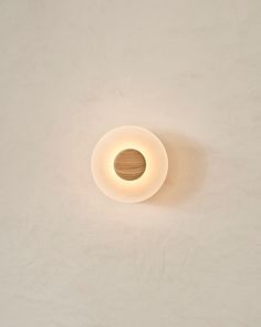 a white wall with a round light fixture on it's side and a wooden object in the middle