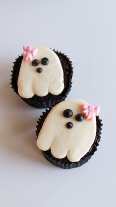 two cupcakes with white frosting and black decorations