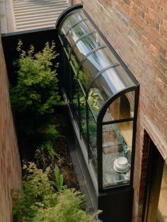 an open window on the side of a building with plants and trees in front of it