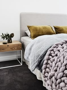 a bed with blankets and pillows on top of it next to a night stand in front of a white wall