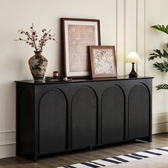 a black cabinet with two vases and pictures on it next to a rug in a living room