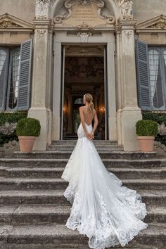 a woman in a wedding dress is standing on some steps and looking at the building