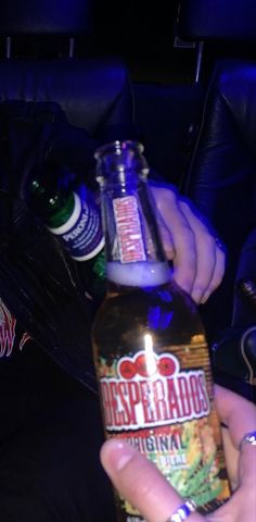 a person holding a beer bottle in their hand with a lit candle on the top