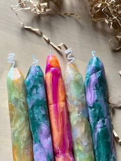 four different colored candles sitting on top of a wooden table next to gold streamers