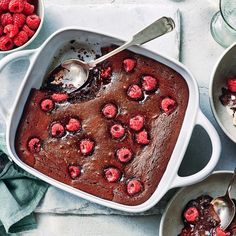 a chocolate cake with raspberries is in a white dish on a table next to other desserts