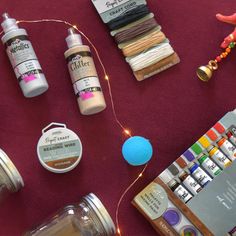 some craft supplies are laying out on a red tablecloth with string lights and other items