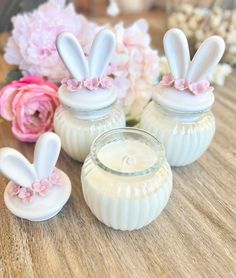 three glass jars with bunny ears sitting on top of a wooden table next to flowers