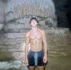 a shirtless man standing in front of a waterfall at the bottom of a cave