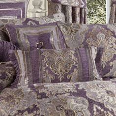 a bed covered in purple and gold bedspreads with pillows on top of them