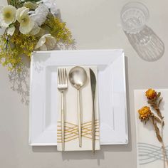 a white plate topped with silverware next to a vase filled with yellow and white flowers