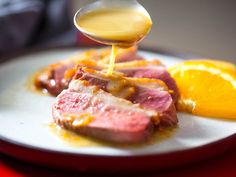 someone is drizzling sauce onto some meat on a plate with orange slices