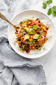 a white bowl filled with rice and vegetables on top of a blue towel next to a wooden spoon