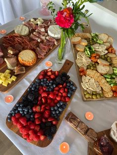 a table topped with trays of food next to candles and vase filled with flowers