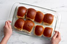 a person holding a plate with mini sandwiches on it and dipping sauce in the middle