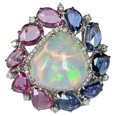 A very beautiful & gorgeous, modern style Ethiopian Opal, Blue Sapphire & Pink Sapphire Cocktail Ring set in 18K White Gold & Diamonds. The weight of the Opal is 9.25 carats. The Opal is of Ethiopian origin and has a green orange play of colour. The weight of the Blue Sapphire Rose Cuts is 3.39 carats. The weight of the Pink Sapphire Rose Cuts is 3.35 carats. Both the Blue & Pink Sapphires are of Ceylon (Sri Lankan) origin. The Diamonds weight is 0.75 carats. Net 18K Gold weight is 8.49 grams. The gross weight of the Ring is 11.84 grams. The dimensions of the ring are 3.00cm x 3.00cm x 1.50cm (L x W x D). The ring is made in US Size 6 and can be changed on request. Features: ✦ Handmade / Handcrafted Fine Jewelry ✦ Gemstone: Ethiopian Opal ✦ Gemstone Cut: Trillion cabochon ✦ Gemstone Weight Luxury Multicolor Opal Ring Fine Jewelry, Luxury Collectible Opal Gemstone Ring, Luxury Pink Sapphire Hallmarked Jewelry, Luxury Pink Multi-stone Sapphire Ring, Luxury Multi-stone Opal Ring Collectible, Sapphire Cocktail Ring, Diamond Cocktail Rings, Sapphire Gemstone, Heel Boots