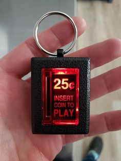 a hand holding a keychain that says 25c insert coin to play