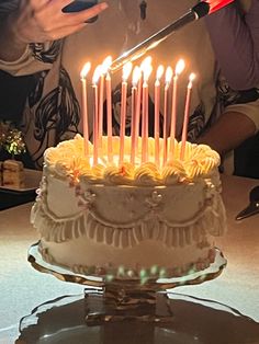 a person cutting into a cake with many lit candles on it and someone holding a cell phone in front of the cake