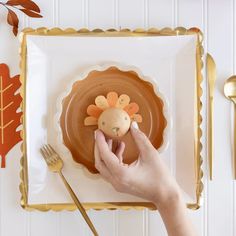 a person holding a small turkey on top of a plate next to a fork and knife