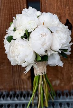 a bouquet of white peonies in front of a wooden door with green stems