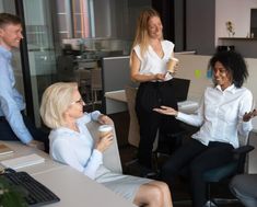 three women in an office talking to each other while one woman holds a coffee cup