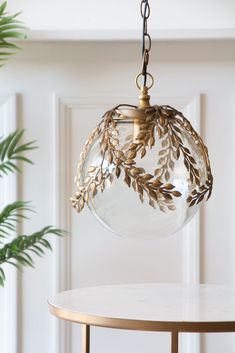 a clear glass ball hanging from a metal frame on a round table next to a potted plant