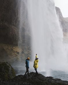 two people are standing in front of a waterfall and looking at the water from below