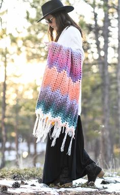 a woman walking in the snow wearing a colorful crochet shawl with tassels