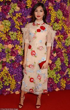 a woman standing in front of a flower wall wearing a dress with flowers on it