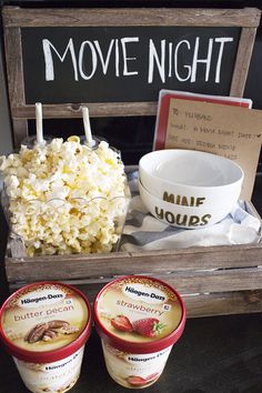 two cups of ice cream next to a bowl of popcorn and a sign that says movie night