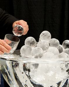 a person is mixing ice cubes into a large glass bowl with water in it