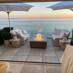 an outdoor fire pit with chairs and umbrellas overlooking the ocean at sunset or sunrise