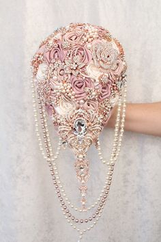 a woman's hand is holding a pink brooch with pearls and flowers on it