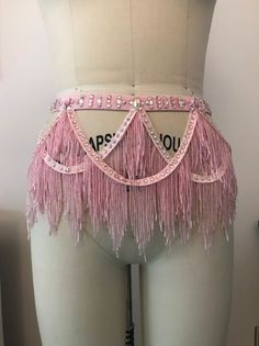 a mannequin with pink fringes and jewels on it's waist, in front of a white wall